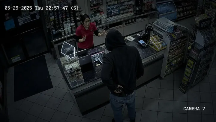 Live camera feed showing a hooded suspect drawing a concealed weapon in front of the counter while an employee stands behind it